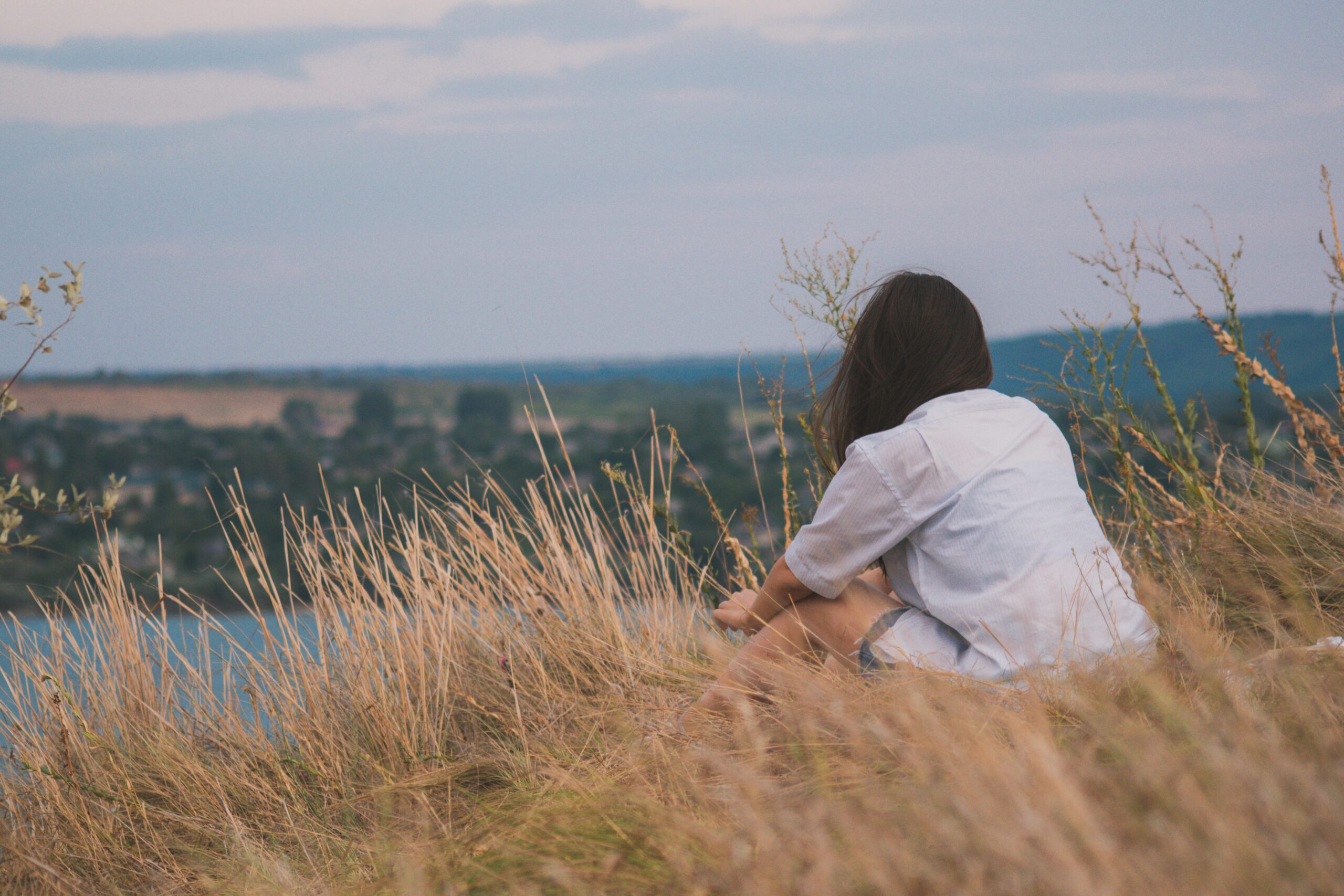 Femme assise au bord d'un champ, regardant l'horizon, illustration d'une vie de fille de ferme et du moment où l'on décide de reprendre ses projets