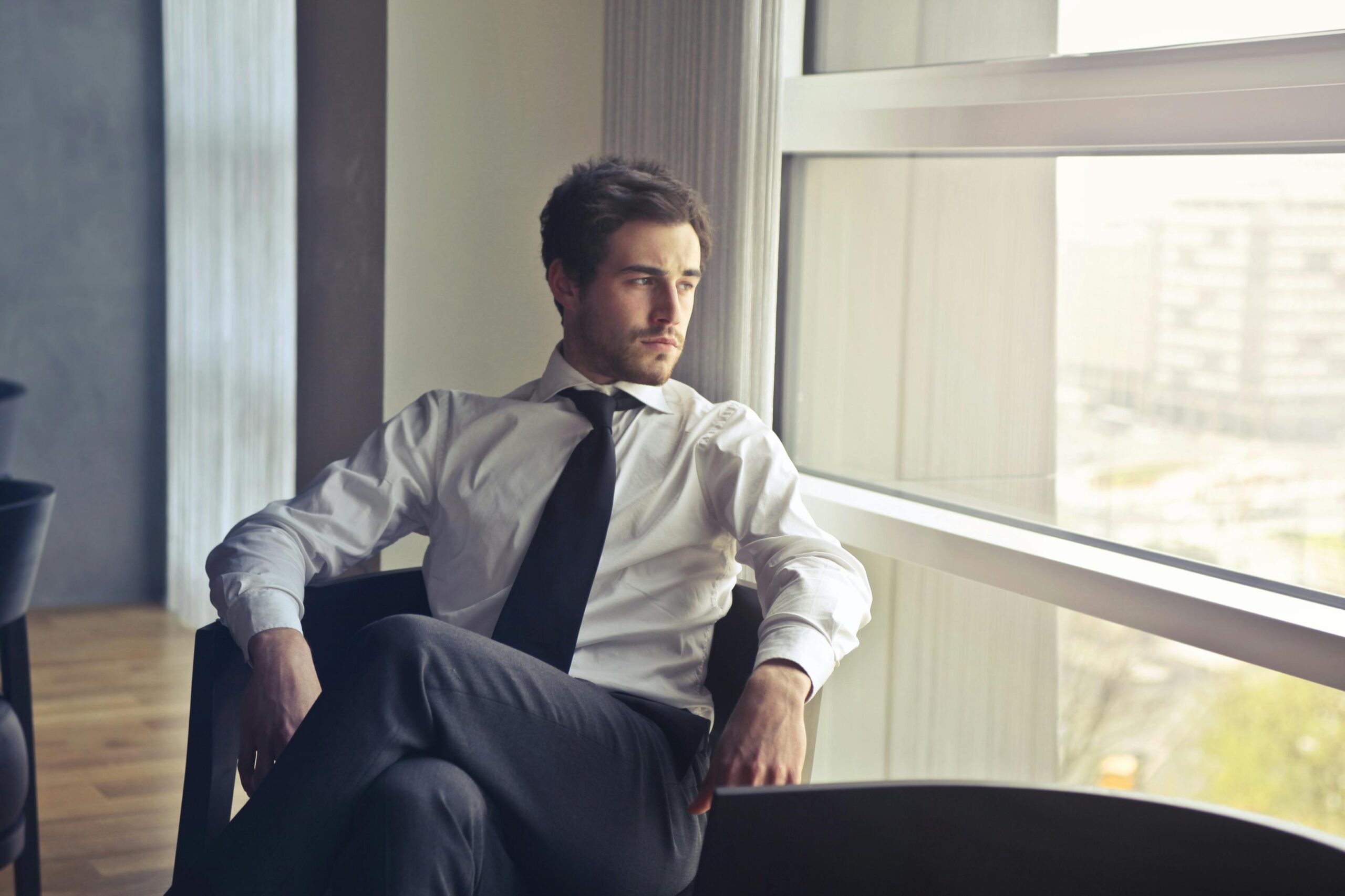 Homme regardant par la fenêtre d'un bureau d'angle, dans une posture pensive, illustration du moment où l'on décide de refuser une promotion pour changer de vie