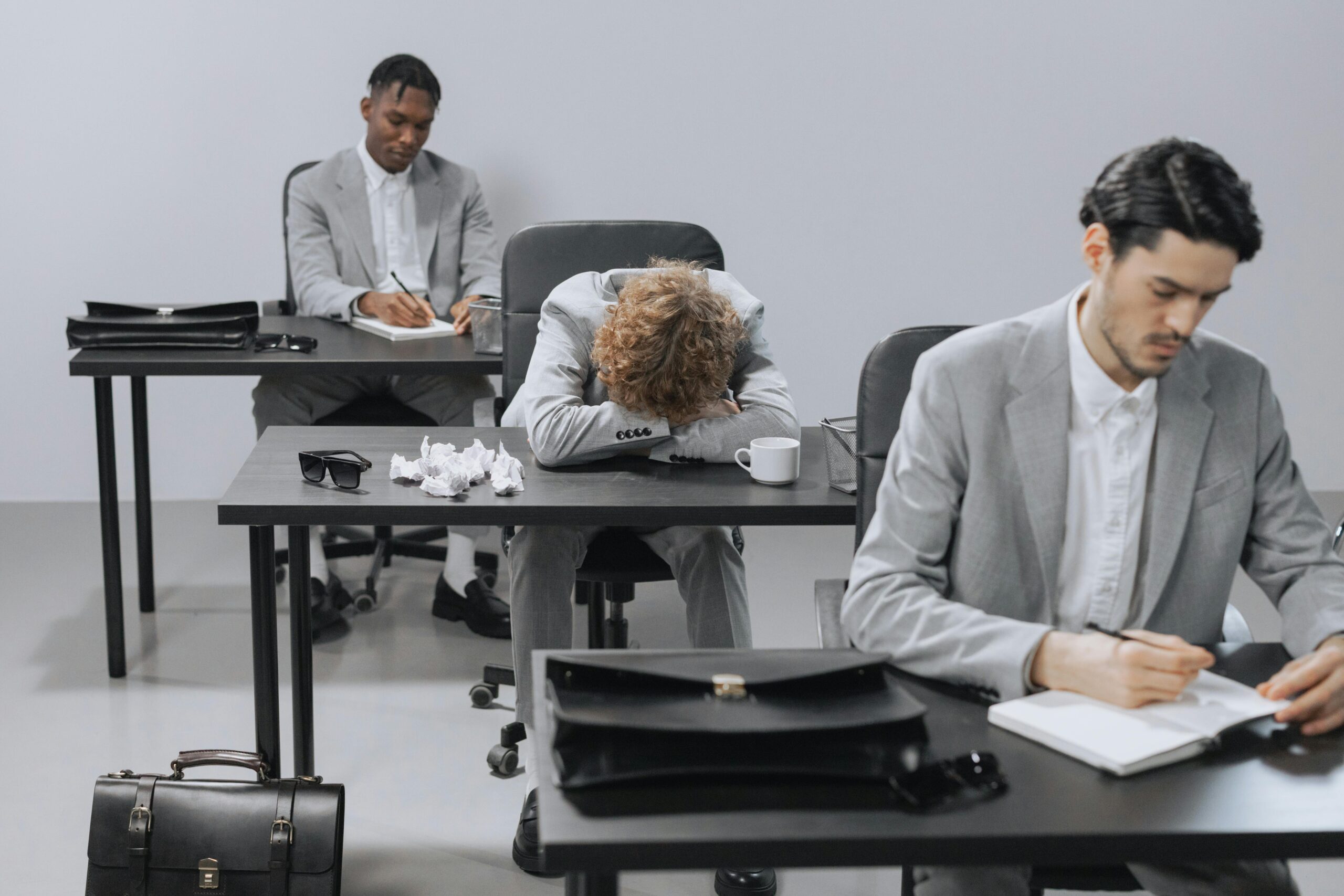 Collaborateur effondré sur son bureau entre deux collègues qui travaillent — illustration du biais de santé au travail en entreprise